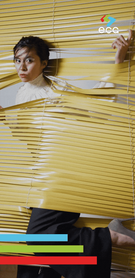 A woman peers through yellow blinds, showcasing vibrant and intentional color correction techniques used in professional video production.