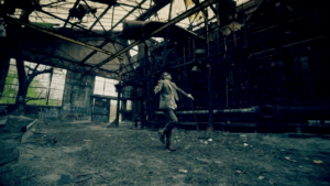 16 OS - 3's Company music video still of a man in a warehouse.