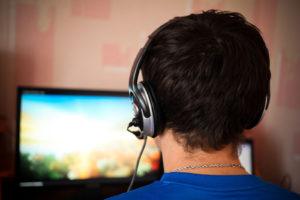 Man at computer playing online video game with headphones