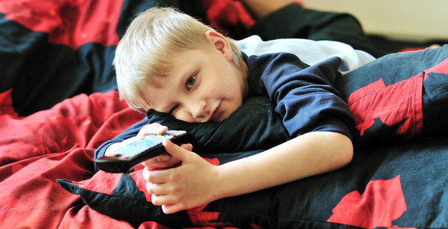 Little boy in bed watching morning cartoons on TV.