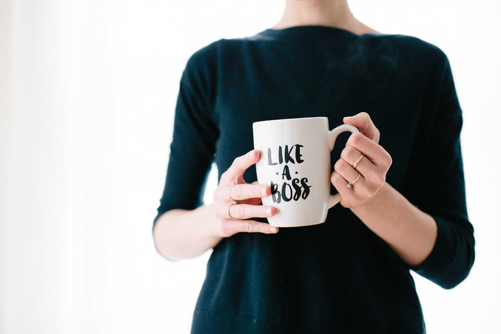 A go-getter woman stands with a coffee cup that says, "Like A Boss".