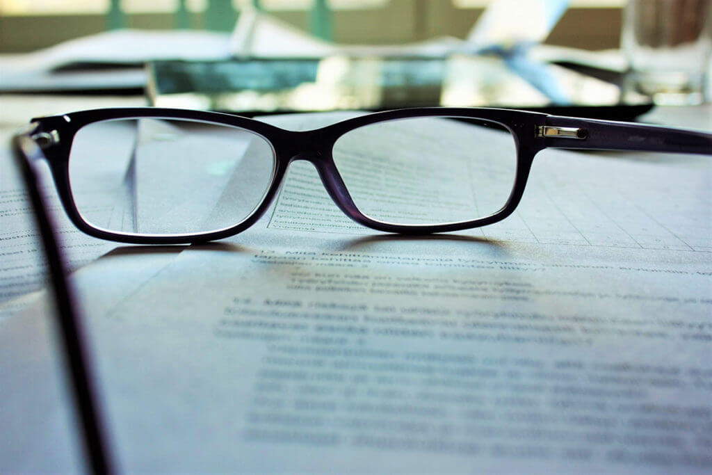 A pair of reading glasses sits on top of a contract for video production.