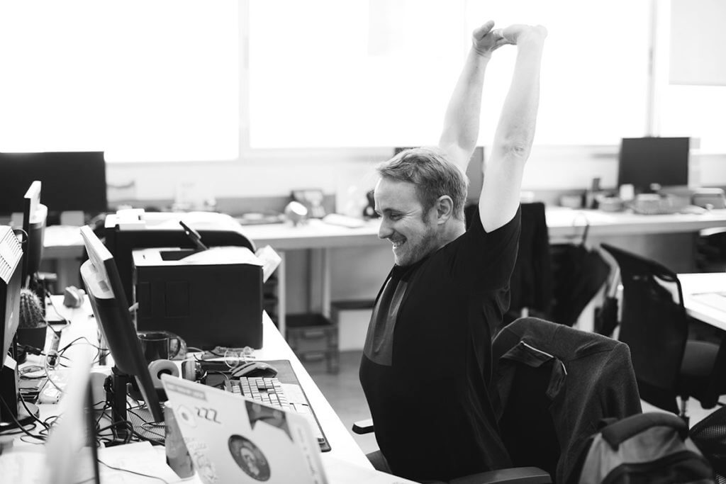 A happy computer guy stretches his arms above his head, happy his is not suffering imposter syndrome anymore.