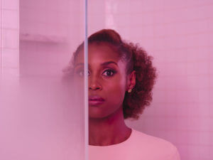 Actress Issa Rae from HBO's Insecure stands behind a glass wall with pink lighting her skin tone.