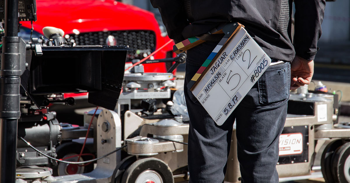 A person with a slate stands in front of equipment parked on set, indicative that locations cost money, baby!