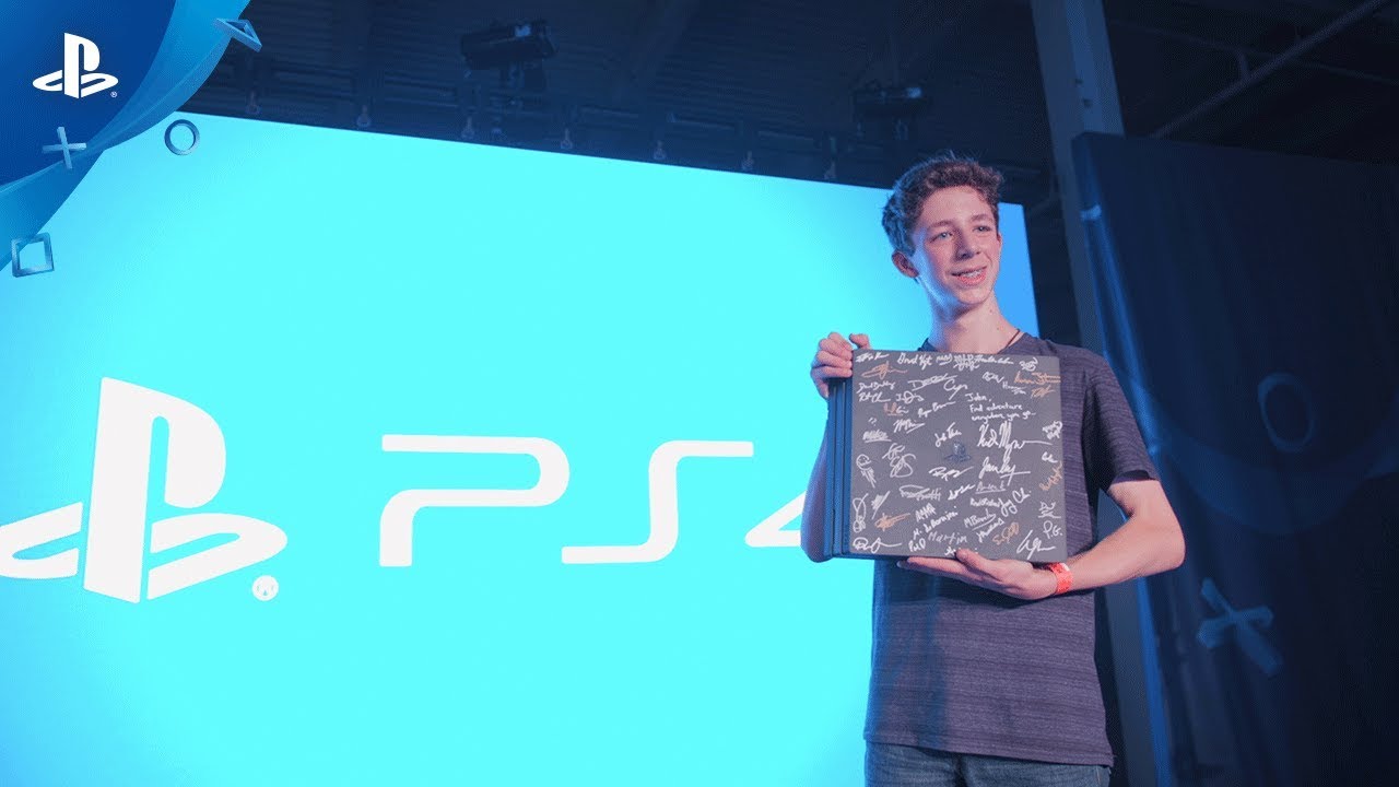 A boy stands in front of a PS4 display and holds a binder, part of the Sony PlayStation - My Road to Greatness (Mooresville, NC) yearly promotion.