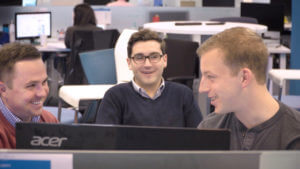 Three QA Symphony employees smile while discussing why they work at QA Symphony.