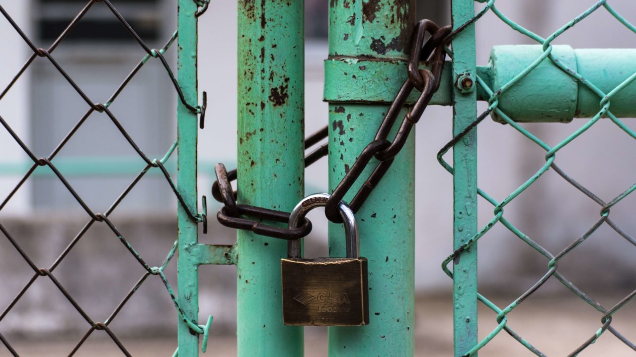 A rusted, green-painted fence and gate with a chain lock.
