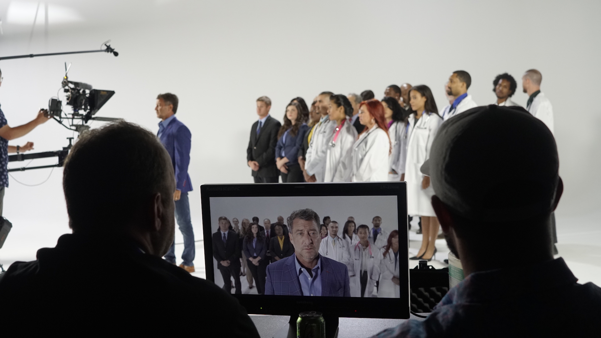 Two production assistants view a cast on a monitor behind the scenes.