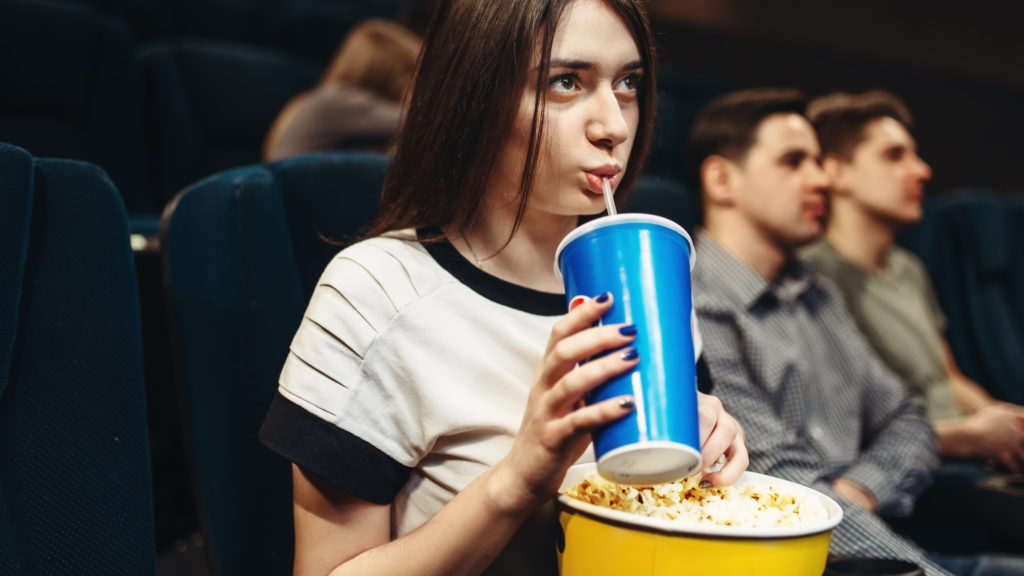 A woman with a beverage and popcorn sits in a movie theater to watch films from herspective.