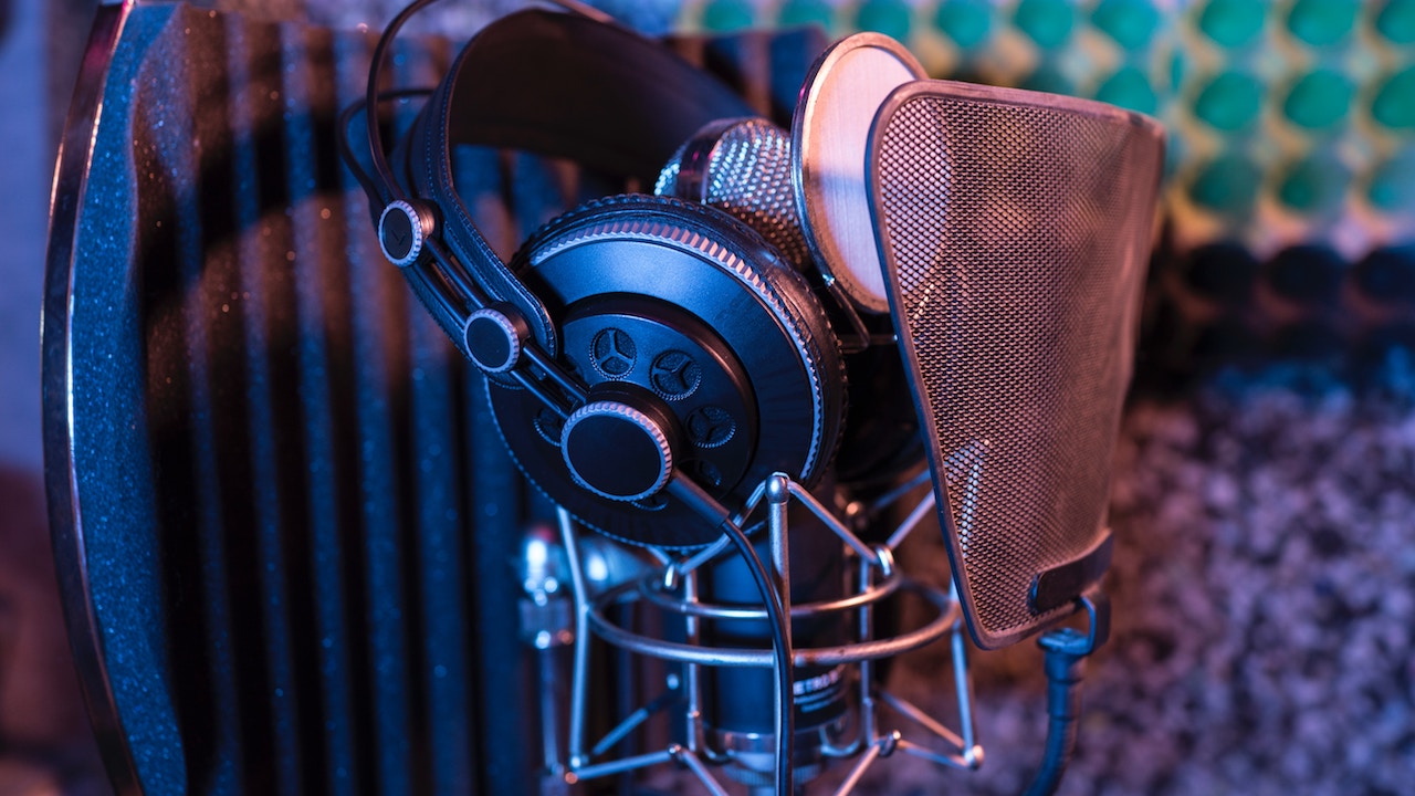 A microphone, pair of headphones, and a sound shield in a recording booth.