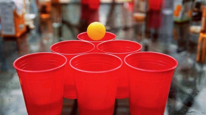 Beer pong game with six red cups in a pyramid and a yellow ball