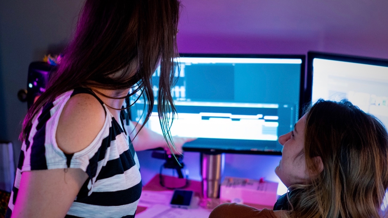 Two women pointing at one of two monitors.