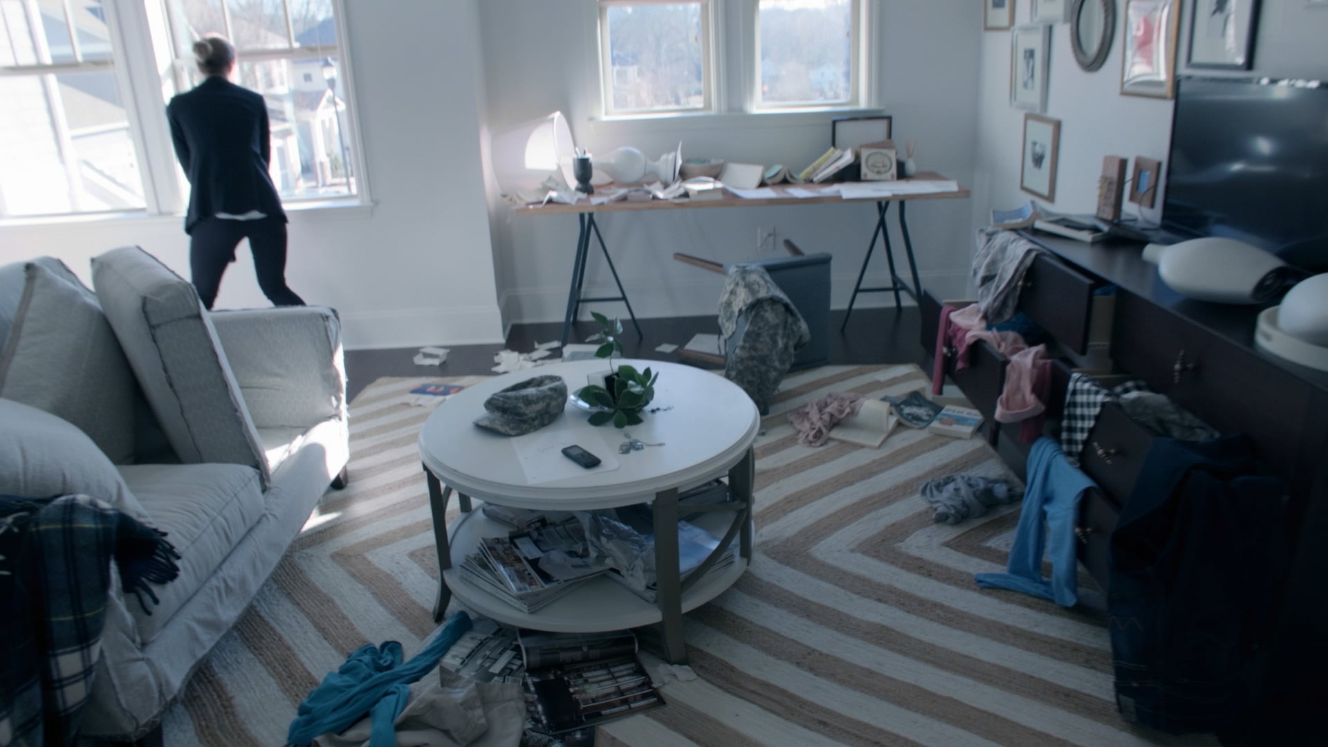 A woman looks out the window of a ransacked living room.