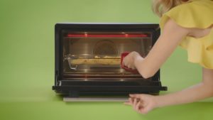 A lady reaches into a smart oven with a red oven mitt.