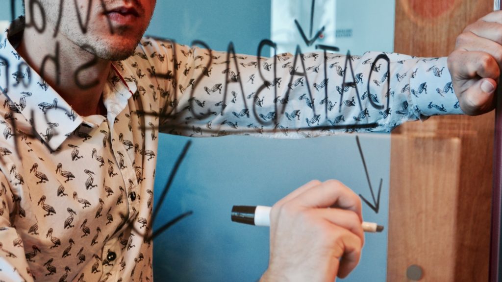 Man writes with black marker on a clearboard