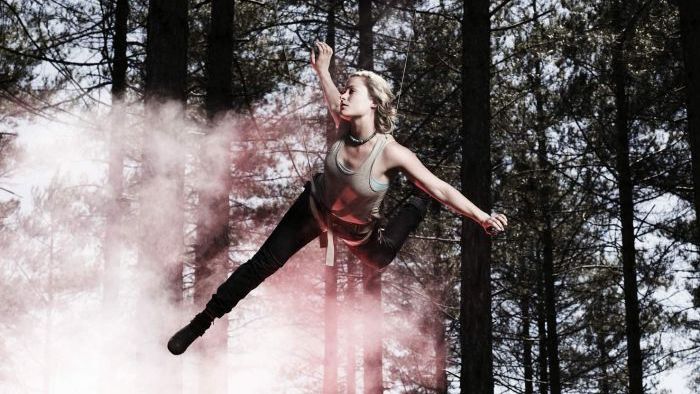 A stunt woman in an action harness mid-air in a forrest