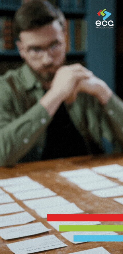 writer leans over a table, studying and rearranging index cards with scenes, emphasizing the planning and organization involved in treatment writing