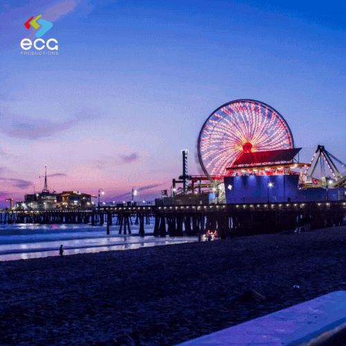 Timelapse of the Santa Monica Pier, shifting from bright daylight to the colorful glow of night, with the Ferris wheel lighting up against the darkening sky. The vibrant scene captures one of LA's most recognizable landmarks, showcasing the type of location a 'Los Angeles fixer' might secure for dynamic day-to-night shots, capturing the energy and atmosphere of Southern California for film and TV productions.