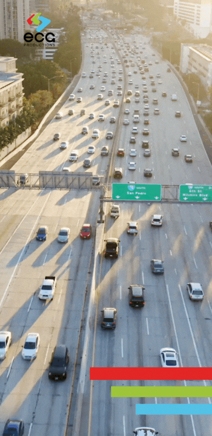 Wide shot of a Los Angeles highway with moderate traffic, cars moving smoothly along multiple lanes against a backdrop of palm trees and city buildings. The scene reflects the vast and complex road networks that a 'Los Angeles fixer' navigates to coordinate film and TV production logistics across the city, ensuring swift access to diverse shooting locations.