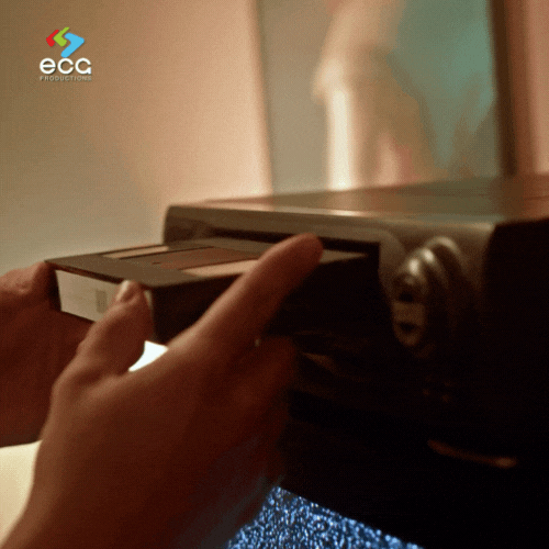 Close-up of hands inserting a VHS tape into a vintage player, with static on the screen—capturing the nostalgic process and care involved in restoring old videos to preserve timeless content.