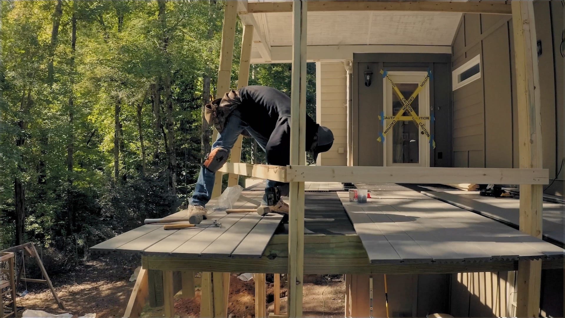 A carpenter works on an elevated patio deck in the backyard.