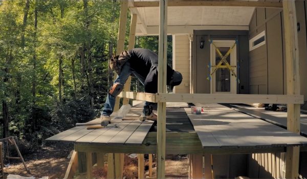 A carpenter works on an elevated patio deck in the backyard.