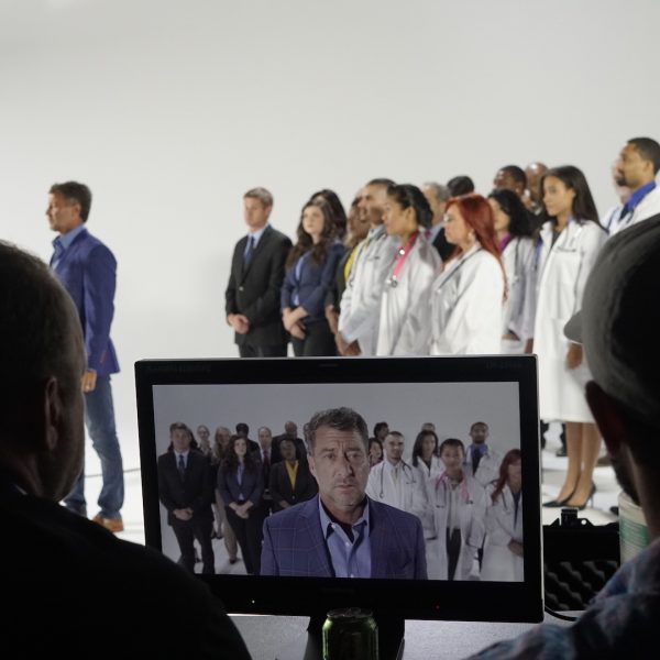 Two production assistants view a cast on a monitor behind the scenes.