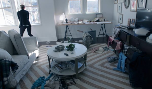 A woman looks out the window of a ransacked living room.