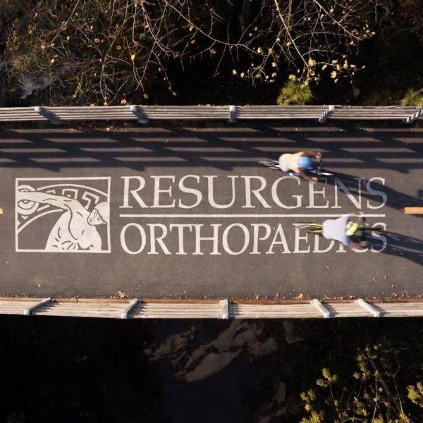 Two cyclists on the Silver Comet Trail pass over the words Resurgens Orthopaedics.