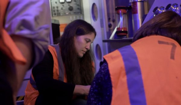 Workers in orange vests squat down as they plan their escape.