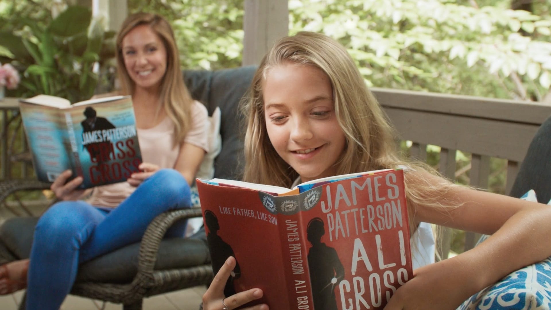 A mother and daughter sit outside on a patio and read Criss Cross and Ali Cross.