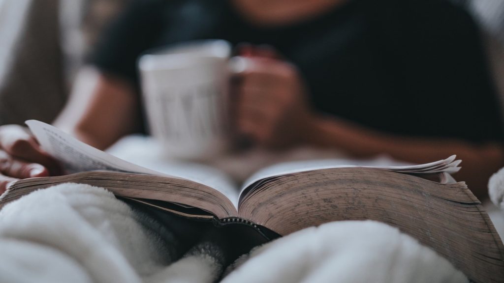 A person stays motivated yet relaxes while reading a book and holding a mug.