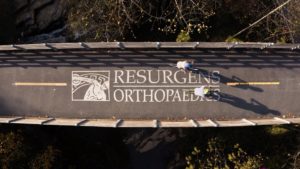 Two cyclists on the Silver Comet Trail pass over the words Resurgens Orthopaedics.