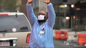 A medical professional standing in the street waves his hands as he keeps reaching.