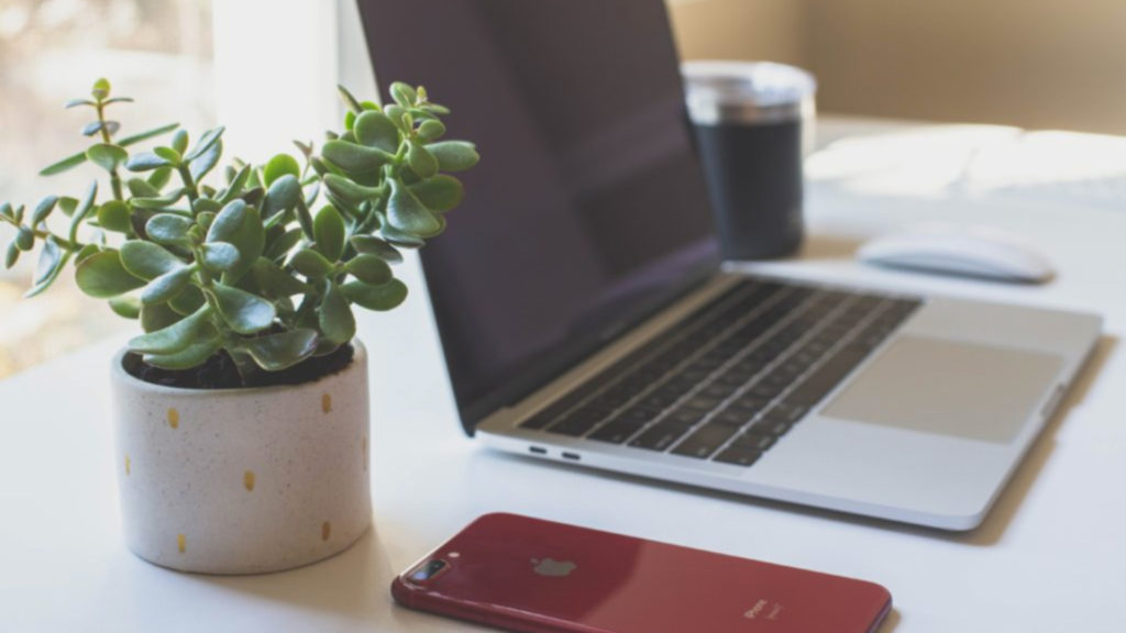 A laptop, mouse, phone, and plant sit on a desk ready for remote training post-pandemic.