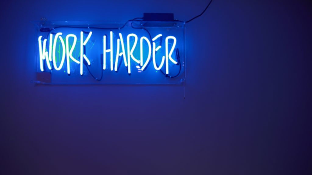 A blue neon sign that says, "Work Harder."